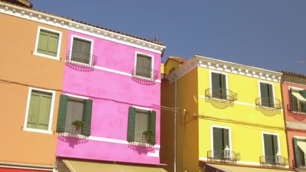 クローズアップ イタリアのブラーノでカラフルな家の白いフレームの窓の壮大なショット 晴れた夏の午後にヴェネツィアの運河に面した見事な家々の美しいファサードに沿って歩く — ストック動画