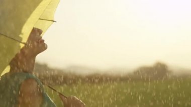 Slow Motion, Close Up: Mutlu genç kadın sakin yeşil bir çayırda ferahlatıcı bahar yağmuru sahiptir. Oyuncu sarışın kız dansları ve Mayıs ayında yağmurlu bir yaz öğleden sonra altın ışıklı doğa etrafında bakar.