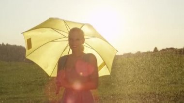 Yavaş Hareket, Portre, Lens Flare: Muhteşem sarışın kadın kırsal pitoresk yağmurlu bir günde kameraya bakarken gülümsüyor. Neşeli kız güzel bir günün tadını çıkarırken bir şemsiye tutar