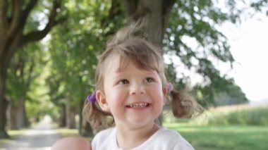 Slow Motion, Close Up: Sevimli bir yüz ile eğlenceli küçük kız onun en sevdiği oyuncak bebek tutarak güneşli cadde etrafında atlar. Mutlu bebek kızı parkta bir aile yürüyüşü sırasında onu bebek ile oynarken