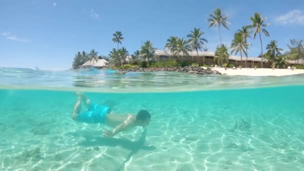 スローモーション ハーフ水中 日当たりの良い熱帯の島の近くに夏の休日ダイビングにアクティブな男 陽気な旅行者は 絵のように美しいエキゾチックな白い砂浜を過ぎて壮大な海で水中を泳ぐ — ストック動画