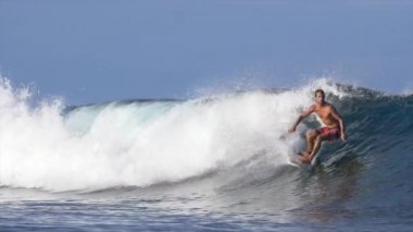 Yavaş Hareket: Pro surfboarder sürmek ve büyük mavi Cloudbreak dalga üzerinden atlar. Atletik erkek sörf tahtasında büyük bir tüp dalga sürmek. Bir yaz öğleden sonra sörf aşırı sporcu Awesome atış.