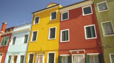 Düşük Açı: Güneşli bir yaz gününde pastoral Burano dünyaca ünlü canlı renkli evlerin nefes kesen görünümü. Venedik, İtalya'daki tarihi kanalların yakınında güzel turuncu ve mavi evlerin önünden yürümek.