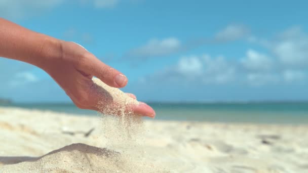 スローモーション クローズアップ レンズフレア 楽園の島のビーチで遊んでいる認識できない女性は 夏の風が彼女の穏やかな手から砂を吹き飛ばします 女の子の把握から飛び出す砂の粒子 — ストック動画