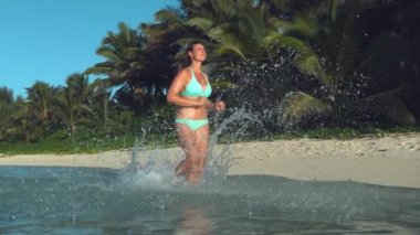 Yavaş Hareket, Düşük Açı: Neşeli kadın turist uzak tropikal adada kumlu kıyıaşağı rahatlatıcı bir koşu için gider. Okyanus suyu Kristal berraklığında damlalar plajyakınında uygun kadın çalışır gibi havada sinek.