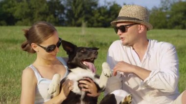 Ağır çekim, Close Up: Kadın sahibi genç çiftin mutlu köpek yavrusu güzel göbek ovmak verir. Neşeli erkek ve kız açık havada bir şirin kenar kömür ocağı köpek bir güneşli yaz gününde eğleniyor.