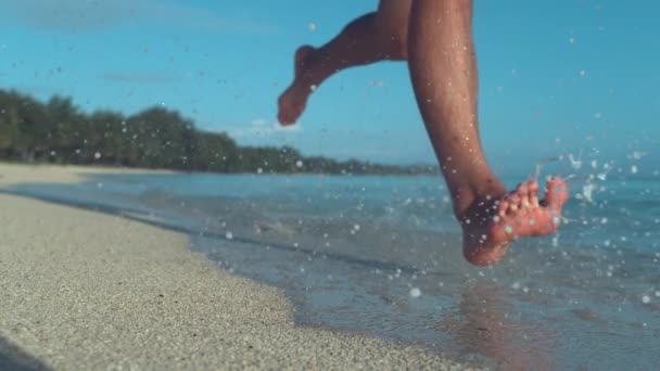 慢动作 低角度 玻璃水滴飞来周围无法辨认的人的脚 因为他跑下阳光明媚的海滩 沿着热带岛屿的白色沙海岸线慢跑的酷镜头 — 图库视频影像