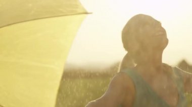 Slow Motion, Close Up: Kaygısız genç sarışın kadın ferahlatıcı bahar yağmuru ona düşmesini sağlar. Yeşil sundress neşeli kız yan şemsiyesini koyar ve serin yaz yağmurda dans.