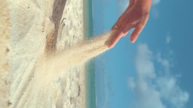 Dikey Yavaş Hareket, Close Up: Tanınmayan kadın beyaz kum bir avuç kaldırır ve Cook Adaları sakin kumlu plajda geri düşmesine izin verir. Tatilde kumla oynayan genç kadın.