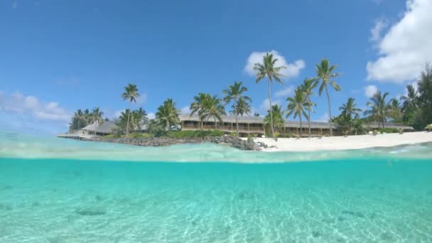 HALF UNDERWATER : Station balnéaire en bois entourée de palmiers et d'un magnifique océan cristallin qui regarde la plage de sable blanc vide des îles Cook. Vue pittoresque de l'hôtel en bord de mer tropical .
