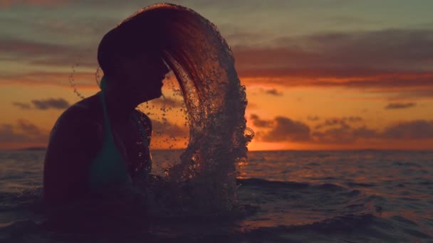 スローモーション クローズアップ シルエット 若い女性は彼女の長い髪を裏返し エキゾチックなビーチで息をのむような夜にガラスの水をはねます 遊び心のある女性旅行者は さわやかな海で涼しみます — ストック動画