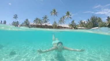 Yavaş Hareket, Yarım Sualtı: Yaz tatilinde aktif genç kadın kameranın önünden şnorkelle doluyor. Pastoral tropik plaja yakın pitoresk camsı okyanus etrafında turkuaz bikini şnorkel kız.