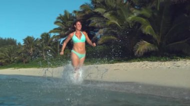 Yavaş Hareket, Düşük Açı: Rahat bir tatile çıkan Kafkas kadını, muhteşem egzotik plaj boyunca cam gibi okyanusta koşar. Bikini neşeli kız güneşli bir akşam sığ suda koşu gider