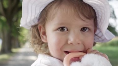 Slow Motion, Portrait, Close Up, Dof: Neşeli küçük kızı, ailesiyle birlikte parkta piknik yaparken kabarık oyuncağa çiğnerken gülümsüyor. Beyaz bir çiğneme oyuncak üzerinde diş sevimli bebek kız diş çıkarma.
