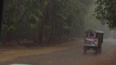 Angkor Wat, Kamboçya, Nisan 2017: Beton yolda seyreden Tuk tuk araçları egzotik ormanın ortasında şiddetli bir yağmur fırtınasına yakalandı. Meşgul Kamboçya kırsal yol yakınında oluşturan büyük su birikintileri