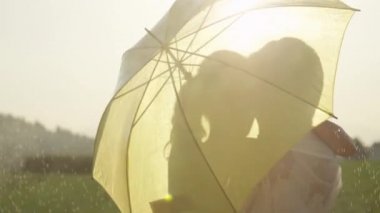 Slow Motion, Close Up, Lens Flare: Aşık erkek ve kadın altın kırsal öpücük gibi şemsiye arkasına gizlemek. Genç Kafkas çift yağmurda dans romantik tarih sırasında durur ve öpücük.