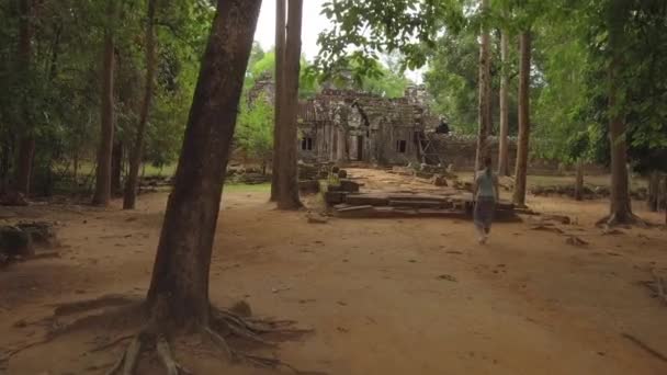 認識できない若い女性は カンボジアの遠い森に建てられた崩壊した寺院の複合体に歩いて行きます 有名なアンコールワット寺院を探索する女性旅行者 宗教的な名残に向かって歩く少女 — ストック動画