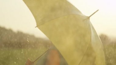 Slow Motion, Close Up: Mutlu kadın şemsiyesi ile döner ve cildinde serin bahar yağmuru hissetmek için kolunu uzar. Muhteşem altın ışıklı bahar doğada güzel sarışın kız dansları.