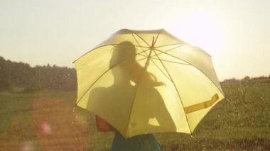 Slow Motion, Close Up, Lens Flare: Yeşil sundress kaygısız sarışın kız onu sarı şemsiye altında yağmurda döner. Altın güneş ışınları ferahlatıcı bir yaz duş eğlenmek gülümseyen kadın parlıyor.