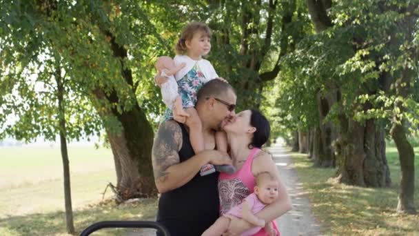 クローズアップ 公園で素敵な春の散歩中に幸せな若い家族の絆 パパの肩に座っている小さな娘は陽気な母親にキスをします 陽気な両親は子供と散歩中にキス — ストック動画
