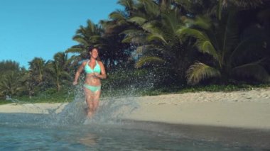 Yavaş Hareket, Düşük Açı: Neşeli Kafkas kadını tropikal denizin sığ kısmında koşarken, camsı su damlacıkları havada uçar. Cennet plajı boyunca koşan aktif dişinin sinematik çekimi.