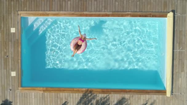 トップダウン シネマグラフ 夏にドーナツフローティに寒いピンクの水着で喜びの女の子 膨脹可能なドーナツの透明なプールの周りに浮かんでいる間 ゴージャスな女性日焼け — ストック動画