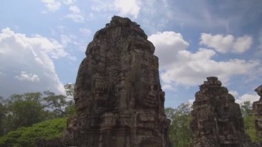Her iki tarafında yüzleri ile muhteşem antik anıtlar güneşli tropikal doğada solmaya. Dünyaca ünlü Angkor Wat tapınak kompleksinde yavaş yavaş çürüyen güzel dini anıtlar. Çarpıcı mimari.