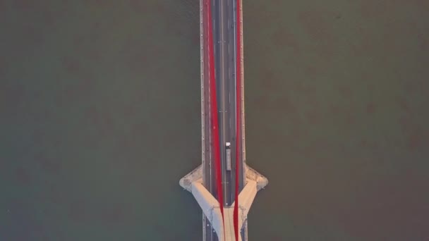 トップダウン 現代の吊り橋を支える大きなコンクリートの柱の上を飛ぶ 大きなアスファルト高速道路を通って濁った水を横断する多数の車やバイクの壮大なショット — ストック動画