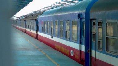 Hoi An, Vietnam, Mart 2017: Uzun kırmızı ve mavi giden ekspres tren Hoi An boş platform bırakır. Yolcu treni güzel Vietnam kırsal tren istasyonundan yola.