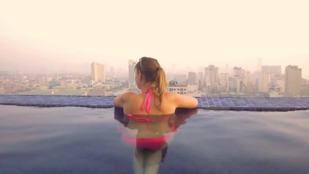 女游客从屋顶游泳池越南的城市 在一个阳光明媚的夜晚 年轻的妇女在暑假中享受放松的游泳池畅游 快乐的女孩在游泳池里放松 — 图库视频影像