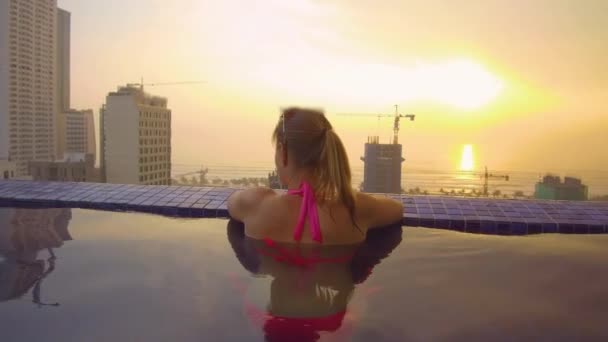 穿着粉色比基尼的年轻女子 在屋顶游泳池欣赏风景如画的热带日落 在一个美丽的夏日夜晚 轻松的女游客在游泳池放松身心 愉快的女孩在假期 — 图库视频影像