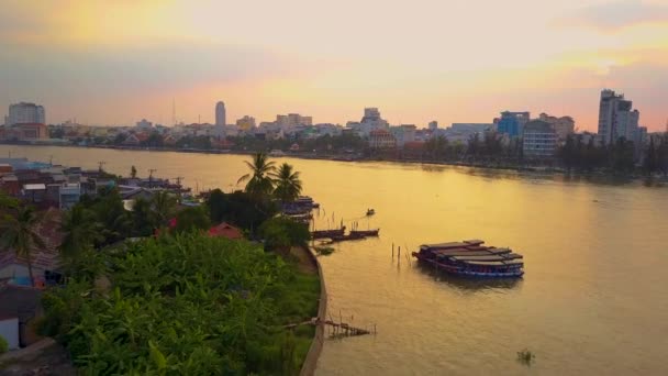 静かな川を渡って小さな地元のボートクルーズは 日没時に大きなベトナムの町に 木製のボートの後ろに飛んで 美しい黄金の夜に牧歌的なウォーターフロントの街に向かって飛ぶ — ストック動画