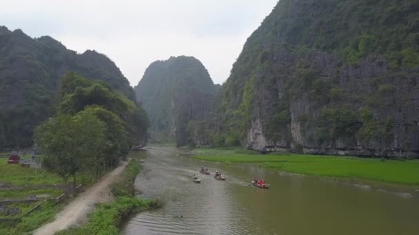 壮大な石灰岩の崖を越えて流れる川を下るボートの観光客 風光明媚なボートに乗る人々のグループは ベトナムの水田を過ぎて行きます 息をのむような田園風景 — ストック動画