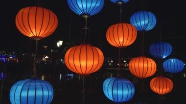 Yakın: Turuncu ve mavi oryantal fenerler Parlatıcı şenlikli bir gece boyunca parlak bir tarihi Vietnamca kasabasında. Güzel Dekoratif lambalar sakin nehrin bir dolunay kutlamaları sırasında aydınlatmak..