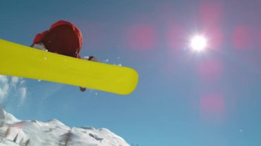 Slow Motion, Close Up, Lens Flare: Parlak güneş profesyonel bir snowboardcuya vuruyor ve pitoresk kış gökyüzü merkezinde bir numara yapıyor. Sürücünün sörf tahtasını havada kaptığı muhteşem bir kare..