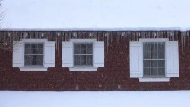 Close Up: Amerika'da Pastoral kırsal ev yoğun bir kar fırtınası sırasında taze kar ile kaplı alır. Büyük ahşap pencereleri olan serin kahverengi bir binanın karlı çatısından sarkan tehlikeli uzun buz sarkıtları.