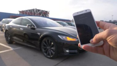 Ljubljana, Slovenya, Mart 2018 - yakın kadar Dof: smartphone Parklar fütüristik uzak tutan kişi Tesla araba kontrol. Harika kendini araba gezinme kendisi boş kırsalda tersten park eder.