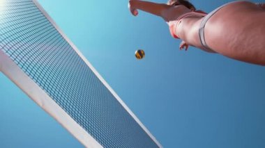 Slow Motion, Bottom Up, Close Up: Plaj voleybolu oynayan atletik beyaz kız havaya sıçrıyor ve topu ağın üzerinden atıyor. Güneşli bir yaz gününde voleybol oynayan genç bir kadın..