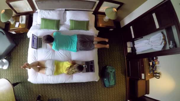タイムラプス トップダウン 大きな快適なベッドに横たわっている間 彼らのラップトップや携帯電話で作業若いカップル 休暇のブログやホテルの部屋の快適さから働くデジタル遊牧民 — ストック動画