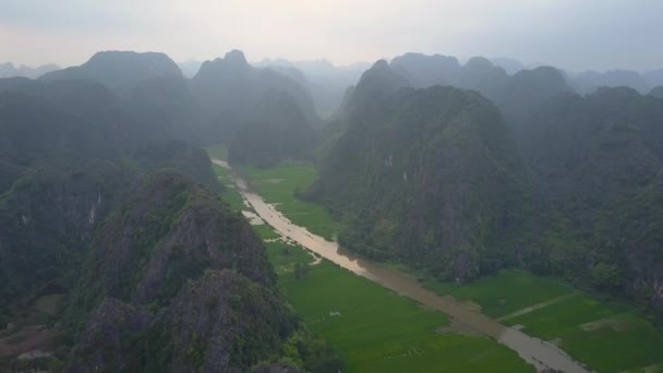 航空写真 ベトナムで緑豊かな岩の多い風景に流れる過去の大規模な濁った川から飛んでいます 石灰岩の崖と霧の風景に川を下って移動ボートの美しい景色 — ストック動画