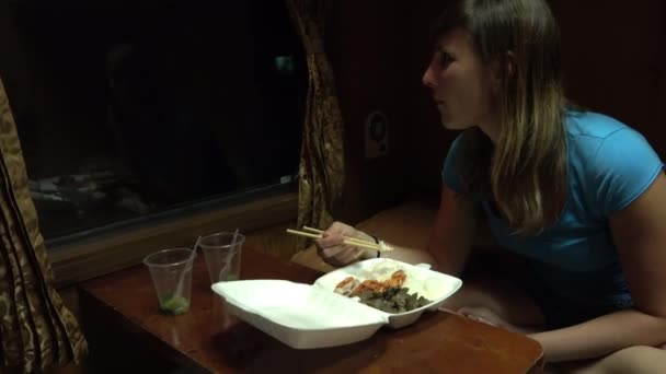 クローズ アップの若い白人女性が夕食の夜行列車で旅行中 女性の観光客が 窓の外見ている寝台列車に乗っている間 お箸で夕食を食べるアジアのバック パッキング — ストック動画