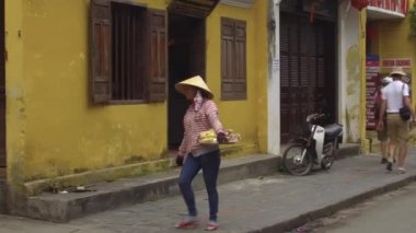 Hoi An, Vietnam, Mart 2017: Hasır şapka takan Asyalı kadın, işlek caddenin karşısında geleneksel Vietnam yemekleri taşıyan bir tepsi taşıyor. Hoi An ziyaret turistlere yerel gıda satan kadın sokak satıcısı.