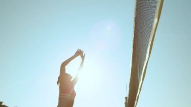 Slow Motion, Lens Flare, Lens Up, Low Angle: Kumsalda voleybol oynayan neşeli atletik kız topu ağlara fırlatıyor. Beyaz kadın tatilleri boyunca erkeklerle voleybol oynuyor..