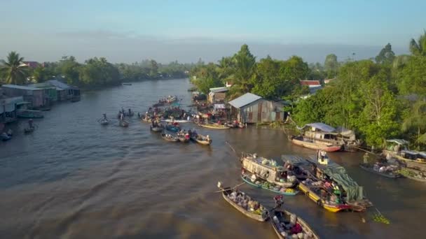 静かなベトナムの田園地帯で泥だらけの川と伝統的な浮遊市場に沿って飛ぶ クールな木製のボートからビジネスを行うアジアの商人の上から壮大なショット — ストック動画