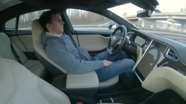 テスラの自動運転車 2018年3月 クローズアップ 若い白人男性が自分の席に背を向け 未来の自動運転車で運転中に眠りにつきます 男性ドライバーは オートパイロットと昼寝に車を設定します — ストック動画