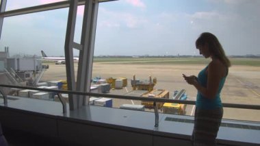 Hanoi Havaalanı, Vietnam, Mart 2017 - Close Up: Vietnam'dan eve dönüş uçağını beklerken akıllı telefonuyla oyun oynayan kafkas kız. Gözlem güvertesi penceresinin yanında duran kadın yolcu.
