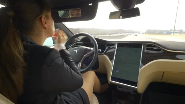 自律型テスラカー 2018年3月 クローズアップ クールな自動運転車で高速道路を走行中にまつげにマスカラを適用する白人女性 仕事に行く途中の若いビジネスウーマンマルチタスク — ストック動画