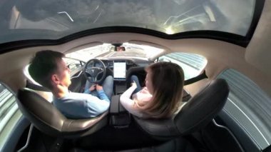 Tesla Autonomous Car, Mart 2018 - Close Up: Kaygısız Beyaz adam ve kadın muhteşem bir otonom Tesla araba güneşli otobanda otururken ve sürüş sırasında sohbet. Yüksek teknolojili araç.