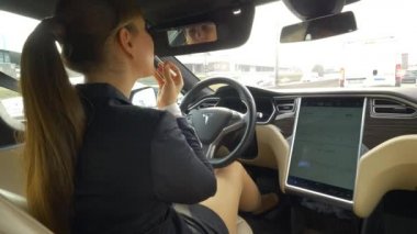 Otonom Tesla Car, Mart 2018 - Close Up: Tesla otomobilini kendi kendine sürerken rujunu süren genç iş kadını. Pervasız kadın sürücü işe gidip onu makyaj yapıyor.