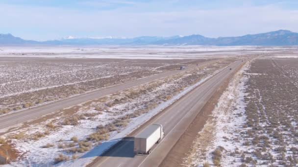 AERIAL: Camión blanco arrastra carga por la autopista escénica que atraviesa el desierto nevado — Vídeo de stock